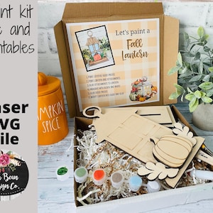May include: A craft kit for painting a fall lantern. The kit includes a wooden lantern, a pumpkin, paint, and instructions. The box is decorated with a fall theme and the text "Let's paint a Fall Lantern".