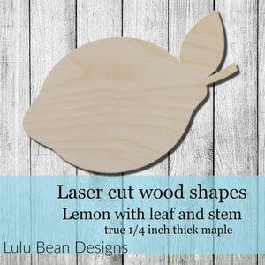May include: A laser-cut wooden lemon shape with a leaf and stem, made from 1/4 inch thick maple. The lemon is light brown and sits on a white and blue wooden background.