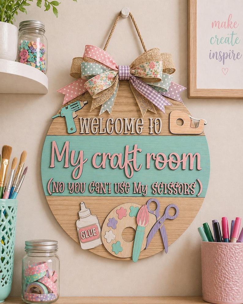 May include: A round wooden sign with the text "WELCOME TO My craft room (NO YOU CAN'T USE MY SCISSORS)". The sign has a large bow at the top and craft-themed embellishments. The sign is hanging on a wall with other craft supplies.