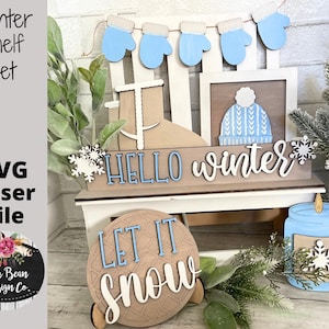 May include: A winter-themed shelf decor set with a wooden sign that says "HELLO winter", a round wooden sign that says "LET IT SNOW", a blue candle jar with a snowflake, and a wooden frame with a blue and white knit hat.