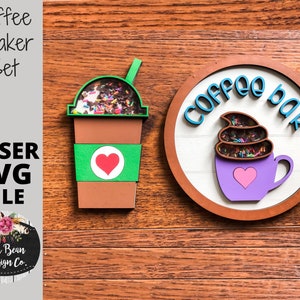 Può includere: Un set di shaker per caffè tagliato al laser con una tazza di caffè marrone con una manica verde e un cuore, e un cartello rotondo che dice "Coffee Bar" con una tazza di caffè viola con un vortice marrone e un cuore.