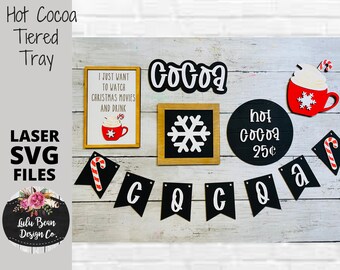 May include: A set of laser cut SVG files for a hot cocoa tiered tray. The design includes a mug of hot cocoa, a snowflake, a sign that says "hot cocoa 25¢", a banner that says "COCOA", and a sign that says "I just want to watch Christmas movies and drink".