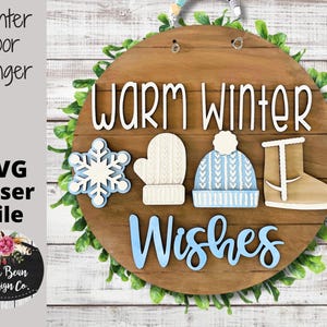 May include: A round wooden door hanger with the text "Warm Winter Wishes" in white and blue lettering. The hanger is decorated with a snowflake, a mitten, a winter hat, and a boot.