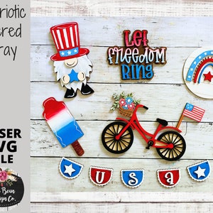 May include: Patriotic tiered tray with a red, white, and blue gnome, a bicycle with a basket of flowers, a popsicle, a rainbow, and a banner that says "Let Freedom Ring".