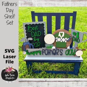 May include: A wooden shelf set with a golf theme. The shelf is blue and gray with a sign that says "Best Dad by Par". There is a golf shirt, a golf ball, and a trophy with the number one and the word "Dad" on it. The shelf also has the words "Happy Father's Day" on it.