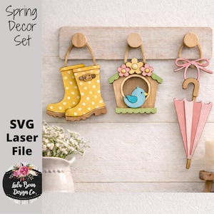 May include: A wooden spring decor set featuring a pair of yellow polka-dot rain boots, a birdhouse with a blue bird, and a pink umbrella. The set is designed for laser cutting and includes the text "Spring Decor Set" and "SVG Laser File".
