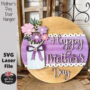 May include: Wooden Mother's Day door hanger with a floral arrangement in a white jar with a purple bow. The words "Happy Mother's Day" are displayed on a purple and white background. The words "Mother's Day Door Hanger" and "SVG Laser File" are also visible.