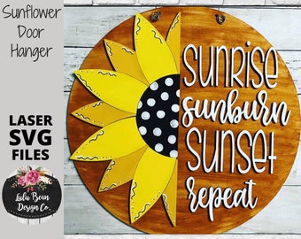 May include: A round wooden door hanger with a yellow sunflower and the text "Sunrise Sunburn Sunset Repeat" in white lettering.