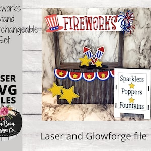 May include: A laser cut fireworks stand with interchangeable signs. The stand is made of wood and has a red, white, and blue theme. The signs are made of white cardstock and have the words "Sparklers", "Poppers", and "Fountains" printed on them. The stand is decorated with stars and fireworks. The image includes the text "Fireworks Stand Interchangeable Set" and "Laser and Glowforge file".