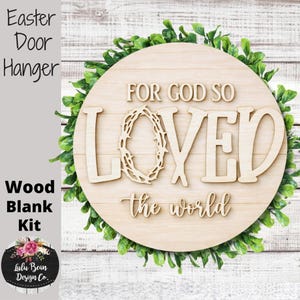 May include: A wooden Easter door hanger kit with the words "FOR GOD SO LOVED the world" in a decorative font. The word "LOVED" features a crown of thorns. The round wooden sign is surrounded by green foliage.