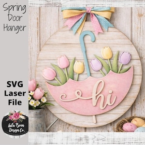 May include: A wooden spring door hanger with a pink umbrella design, featuring tulips and the word "hi". The round sign has a pastel colour scheme and is topped with a multi-coloured bow. The text "Spring Door Hanger" is visible.