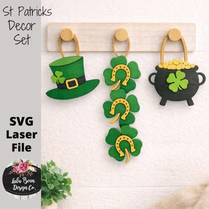 Może przedstawiać: Zestaw dekoracji na Dzień Świętego Patryka z zielonym kapeluszem krasnoludka, koniczynami z podkowami i garnkiem złota. Wycięcia z drewna są pomalowane na zielono, żółto i czarno. Widoczny jest tekst "St Patricks Decor Set".