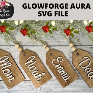 May include: Four wooden gift tags with the names "Mom", "Noah", "Emma", and "Dad" written in white cursive font. The tags are hanging from a string of white lights and a garland of pine branches with red berries.