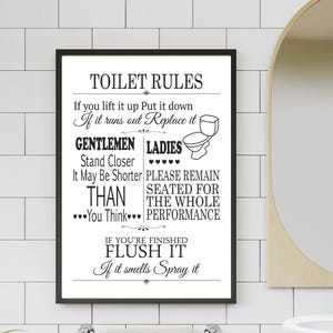 Puede incluir: Un letrero enmarcado en blanco y negro con el texto "TOILET RULES" e instrucciones humorísticas para la etiqueta del baño. El letrero está colgado en una pared de azulejos blancos sobre un toallero con dos toallas grises.
