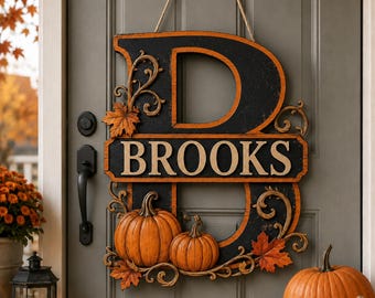 May include: A black and orange wooden door sign shaped like the letter B with the name BROOKS in white lettering. The sign features decorative scrollwork, orange maple leaves, and two orange pumpkins attached to the front of the letter.