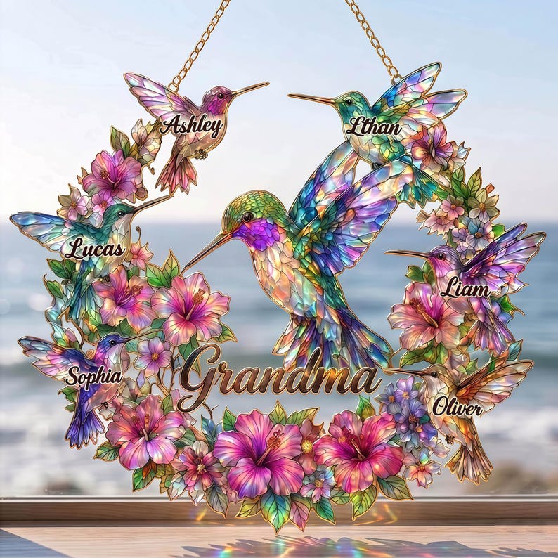 May include: A decorative hummingbird wreath with the word "Grandma" in the center. The wreath features colorful hummingbirds and flowers, with names like Ashley, Ethan, Lucas, Liam, Oliver, and Sophia. The wreath is suspended by a gold chain.