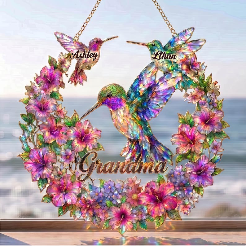 May include: A decorative hummingbird wreath with the names "Ashley" and "Ethan" on the birds. The word "Grandma" is written in cursive. The wreath is surrounded by pink, purple, and blue flowers, with a gold chain for hanging.