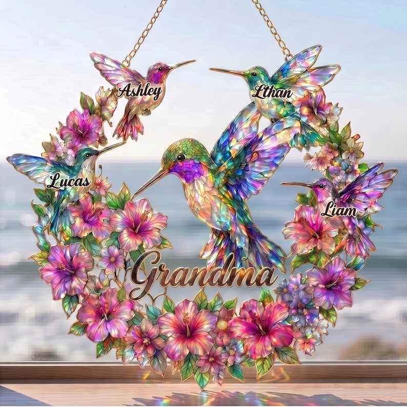 May include: A decorative hummingbird wreath with the word "Grandma" in the center. The wreath features five colorful hummingbirds, each with a name above it: Ashley, Ethan, Lucas, and Liam. The wreath is surrounded by vibrant pink and purple flowers.