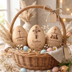 May include: A woven basket holds three wooden Easter eggs with engraved crosses and names: Elijah, Sophia, and The Parker Family. Each egg has a unique design, including a cross, bunny, and floral accents. The eggs are surrounded by decorative elements.