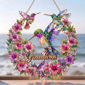 May include: A decorative hummingbird wreath with the names Ashley, Ethan, and Mia. The wreath features colorful hummingbirds and flowers in shades of pink, purple, and green. The word "Grandma" is written in gold script.