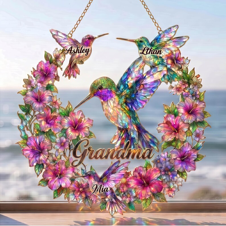 May include: A decorative hummingbird wreath with the names Ashley, Ethan, and Mia. The wreath features colorful hummingbirds and flowers in shades of pink, purple, and green. The word "Grandma" is written in gold script.