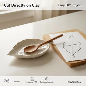 Pode incluir: Um descanso de colher de cerâmica em forma de folha com uma colher de madeira. Um modelo de folha de papel repousa sobre uma tábua de cortar de madeira. Os textos "Cut Directly on Clay" e "Easy DIY Project" são visíveis. O descanso de colher é salpicado.