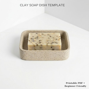 Puede incluir: Un jabonera de arcilla beige con textura moteada contiene una pastilla de jabón rectangular. El jabón es de color beige claro con semillas y hierbas visibles. El texto "CLAY SOAP DISH TEMPLATE" está en la parte superior. El texto "Printable PDF • Beginner Friendly" está en la parte inferior.