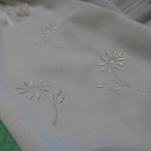 Könnte beinhalten: Weißer Stoff mit gestickten weißen Blumen. Der Stoff hat eine glatte Textur.
