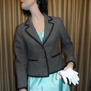 May include: A gray blazer with black trim and a single-breasted button closure. The blazer has a pocket on the left side and is cropped at the waist.