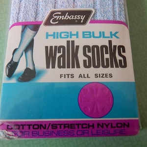 Puede incluir: Un paquete de calcetines de paseo Embassy high bulk en azul claro. El envase incluye el texto Embassy, HIGH BULK, walk socks, FITS ALL SIZES y COTTON/STRETCH NYLON FOR BUSINESS OR LEISURE, con una ilustración de piernas con calcetines.
