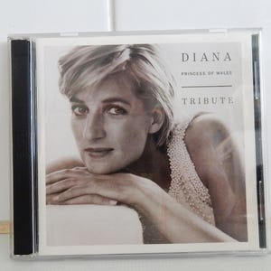 May include: CD case with a monochrome image of Diana, Princess of Wales. The cover displays the text "DIANA PRINCESS OF WALES TRIBUTE". The image shows Diana looking at the viewer. The CD case is in a clear plastic case.