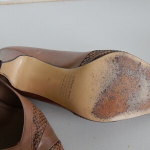 May include: Brown leather heeled shoes with a snakeskin pattern on the toe and heel. The shoes are size 38 and say "Leather Upper Leather Lining Made in Italy" on the sole.