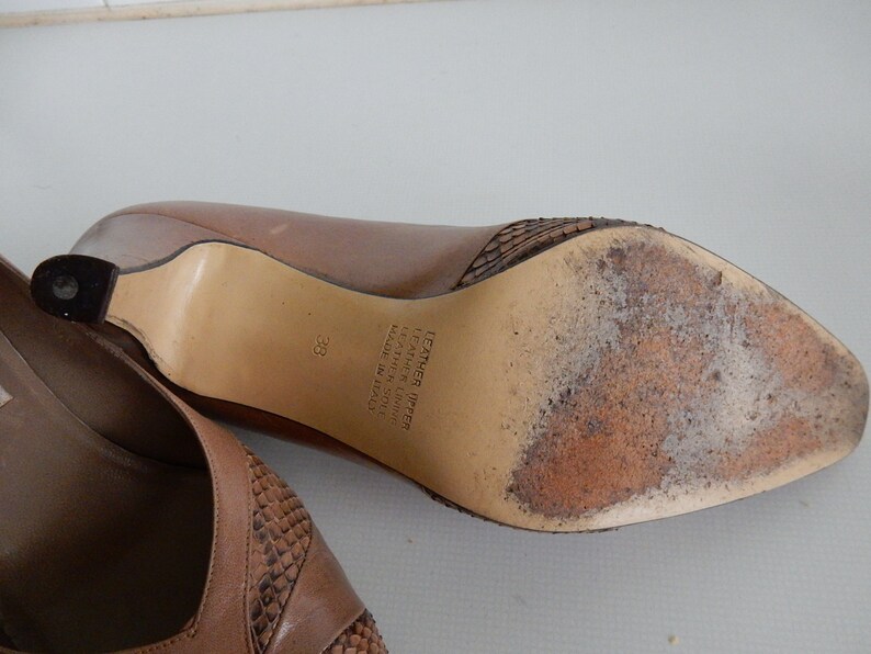 May include: Brown leather heeled shoes with a snakeskin pattern on the toe and heel. The shoes are size 38 and say "Leather Upper Leather Lining Made in Italy" on the sole.