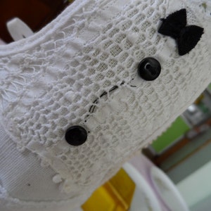 May include: White lace fabric with black buttons and a black bow. The fabric has a delicate, crocheted pattern.
