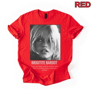May include: A red t-shirt featuring a black and white portrait of Brigitte Bardot. The text "BRIGITITE BARDOT" is below the image, along with a quote about beauty, youth, wisdom, and animals. The word "RED" is in the top right corner.