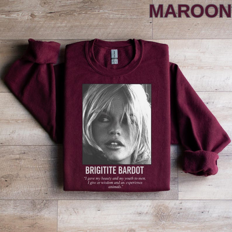 May include: Maroon sweatshirt featuring a black and white image of Brigitte Bardot. The image includes the text "BRIGITITE BARDOT" and a quote about beauty, youth, wisdom, and animals. The sweatshirt is a solid maroon color.
