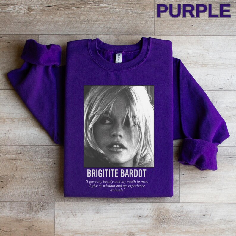 May include: A purple sweatshirt featuring a black and white image of Brigitte Bardot. The image includes the text "BRIGITITE BARDOT" and a quote about beauty, youth, wisdom, and animals. The word "PURPLE" is at the top.