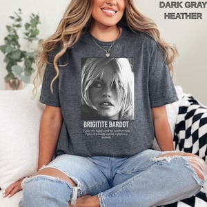 May include: Dark gray heather t-shirt featuring a black and white image of Brigitte Bardot. The text "BRIGITITE BARDOT" is below the image, along with a quote. The shirt is a casual style.