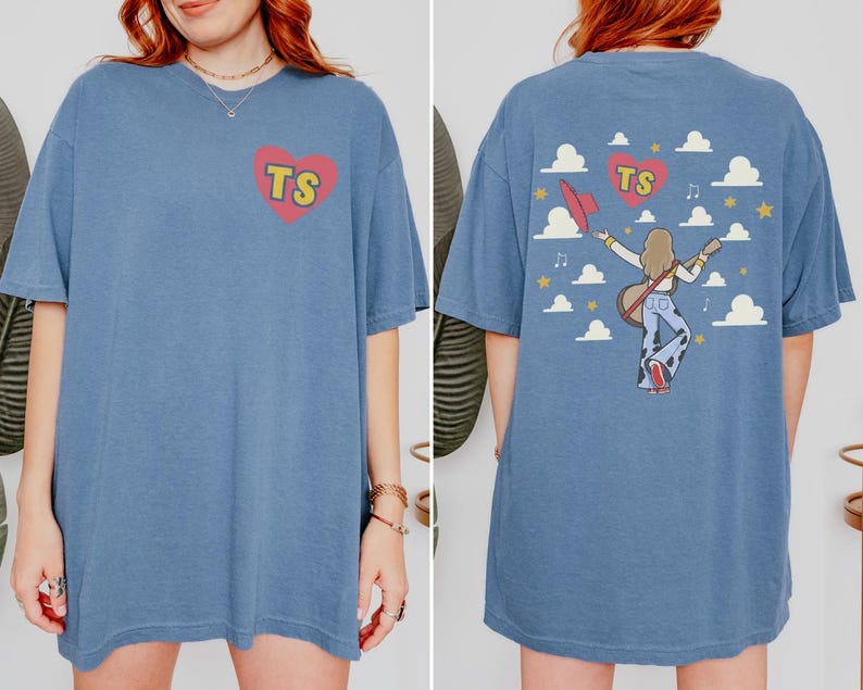 May include: A blue short-sleeve t-shirt featuring a red heart with the yellow letters TS on the front chest. The back displays a graphic of a person with long hair playing a guitar, a red hat, clouds, stars, musical notes, and a red heart with TS.