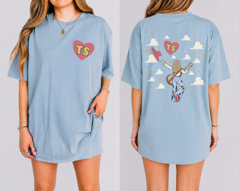 Graphic Comfort Colors t-shirt featuring a TS heart logo on the front and a concert-themed girl carrying a guitar with clouds and stars artwork on the back.