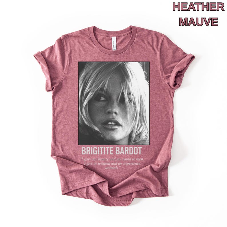 May include: Heather mauve t-shirt featuring a black and white image of Brigitte Bardot. The image is framed with the text "BRIGITITE BARDOT" and a quote. The shirt is a solid color and has short sleeves.