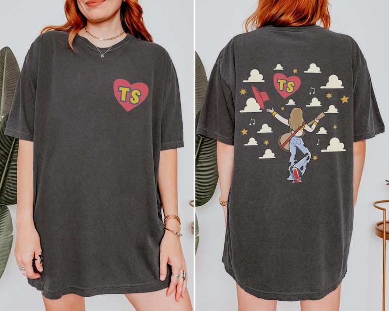 Graphic Comfort Colors t-shirt featuring a TS heart logo on the front and a concert-themed girl carrying a guitar with clouds and stars artwork on the back.