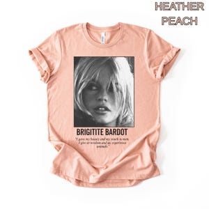 May include: Heather peach-colored t-shirt featuring a black and white image of Brigitte Bardot. The text "BRIGITITE BARDOT" is below the image, along with a quote about beauty, youth, wisdom, and animals.
