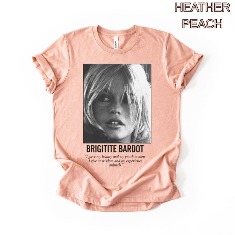 May include: Heather peach-colored t-shirt featuring a black and white image of Brigitte Bardot. The text "BRIGITITE BARDOT" is below the image, along with a quote about beauty, youth, wisdom, and animals.