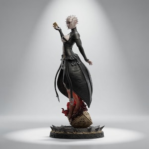 May include: A detailed figurine of a pale, pin-headed character wearing a black leather-like outfit with a high collar and flared skirt. The figure holds a small gold cube, stands atop a larger ornate cube, and rests on a dark, spiked circular base.
