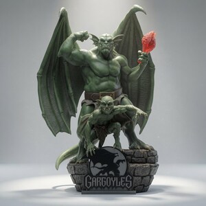 Puede incluir: Una figura de gárgola verde que muestra una criatura alada grande de pie detrás de una criatura más pequeña agachada. La figura grande sostiene un objeto rojo en una mano. La base es un pedestal de piedra con una placa negra que dice GARGOYLES.