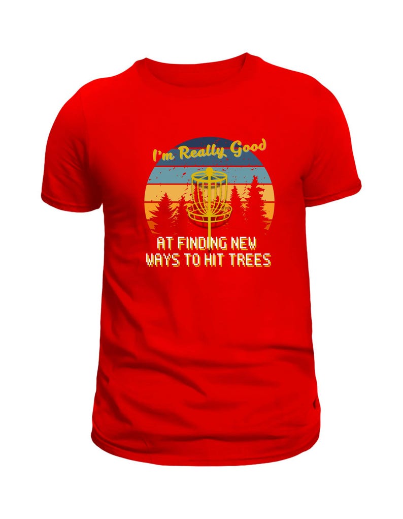 Op de afbeelding: Rood t-shirt met een grafisch ontwerp voor discgolf liefhebbers. Het ontwerp toont een discgolfmand, bomen en de tekst "I'm Really Good At Finding New Ways To Hit Trees" in retro stijl.