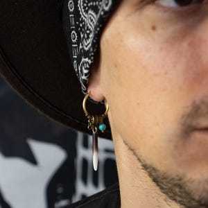 Könnte beinhalten: Ein Creolen-Ohrring mit metallischem Bronzefinish, einer kleinen türkisfarbenen Perle und einem hängenden, stiftförmigen Anhänger mit einem Farbverlauf von Dunkelbraun an der Oberseite bis zu einer weißen Spitze, befestigt an einem Metallring.