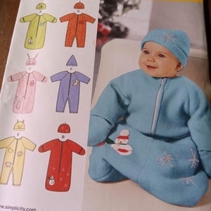 Könnte beinhalten: Ein Schnittmuster zum Nähen von Babyschlafsäcken. Das Muster enthält fünf verschiedene Designs, jedes mit einem anderen Tier- oder Feiertagsmotiv. Das Muster ist von Simplicity und einfach zu nähen. Die Musternummer ist 1565A.