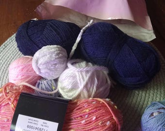 May include: A close-up of a collection of yarn balls in various colors, including pink, white, blue, and orange. The yarn is arranged on a gray surface. The label on one of the balls reads "Color Name: 1005, Color Code: Clean, Code No: 7129341009".